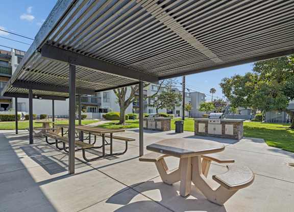 A patio with tables and benches under a striped awning.
