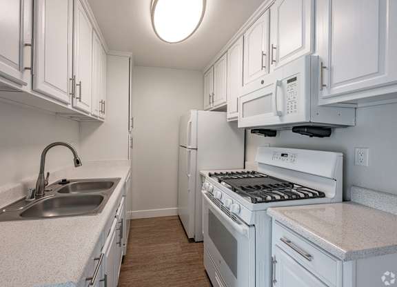 A white kitchen with a sink, stove, and refrigerator at Oak Park Apartments, Monrovia, 91016