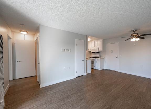A room with a ceiling fan and a kitchenette in the background at Oak Park Apartments, Monrovia, 91016