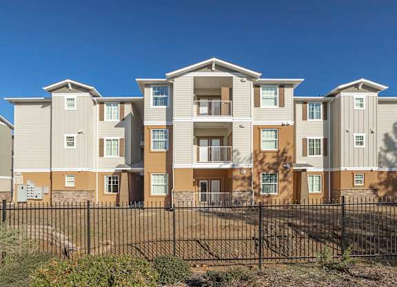 A row of modern townhouses with balconies and a black fence in front.