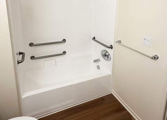 A white bathtub with silver grab bars in a small bathroom.