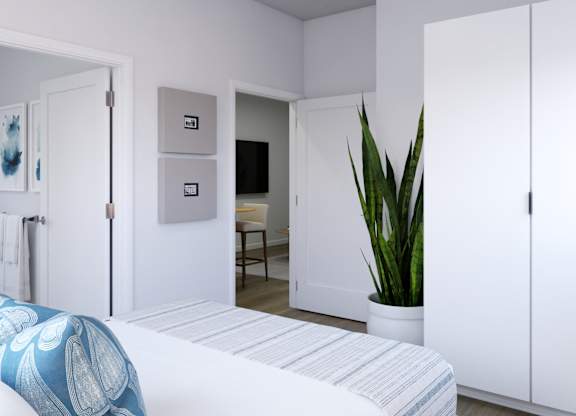 A white bedroom with a bed, a chair, a plant, and a painting on the wall.