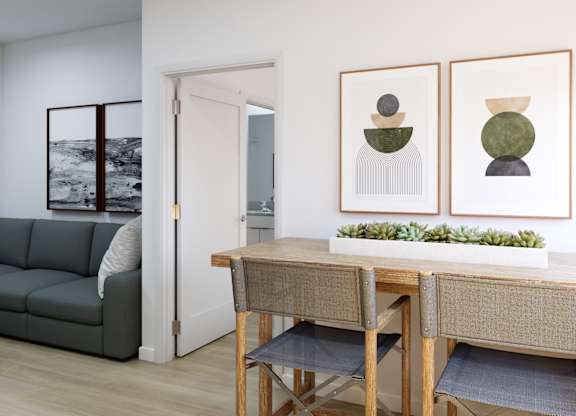 A room with a grey couch, a wooden table and two framed pictures on the wall.
