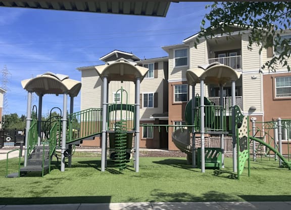 A playground with a green slide and a brown building in the background.
