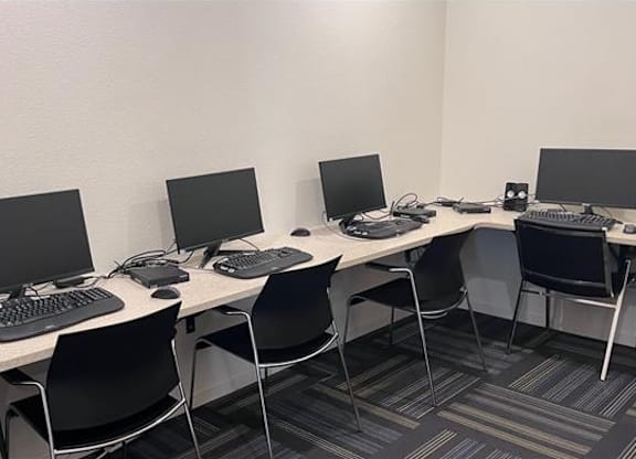 A room with a white desk and black chairs with a computer on it.