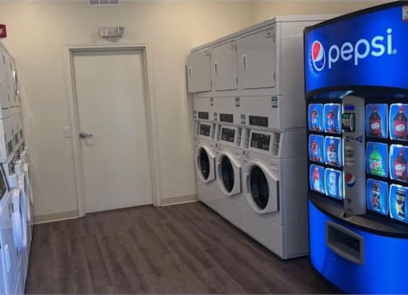 A Pepsi vending machine sits next to a row of washing machines.
