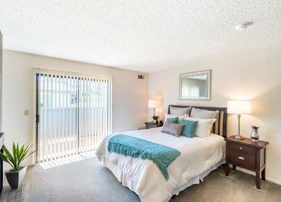 A bedroom with a large bed and a balcony with a sliding door at Chaparral Apartments, Palmdale 93551