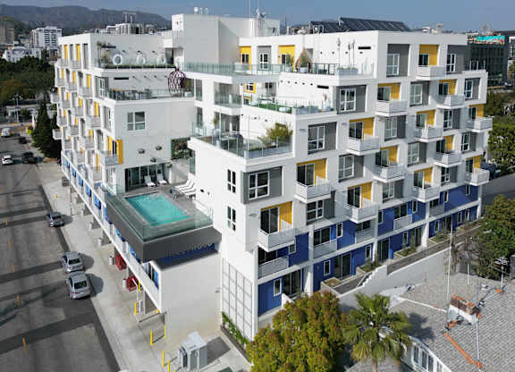 an aerial view of a white building with blue and yellow windows and a pool in front of