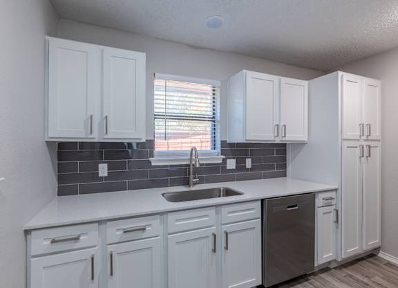A kitchen with white cabinets and a grey backsplash.