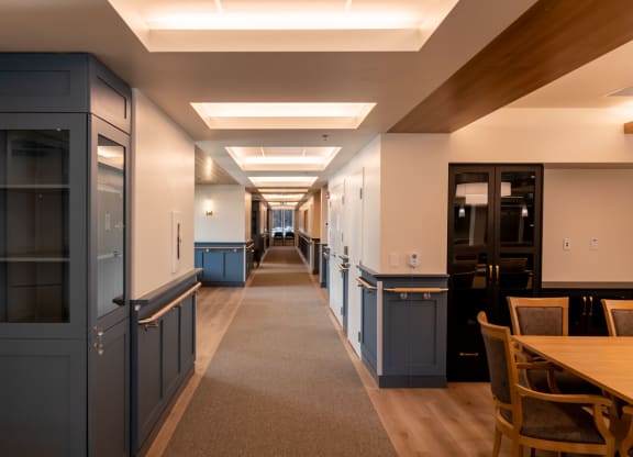 a long corridor with tables and chairs on one side and blue cabinets on the other