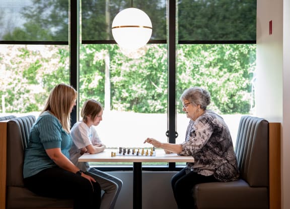 a woman and two children sit at a table playing a game of chess