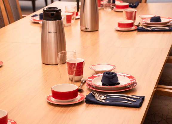 a long table with red plates and cups and a coffee thermos on it