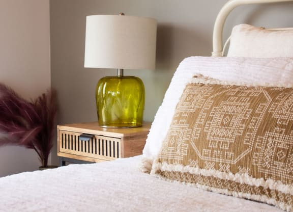 a bedroom with a white bedspread and a green lamp on a wooden nightstand