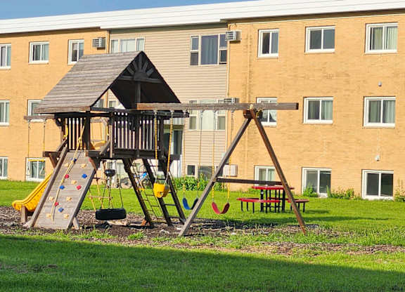 A playground with a swing set and slide in front of a building.