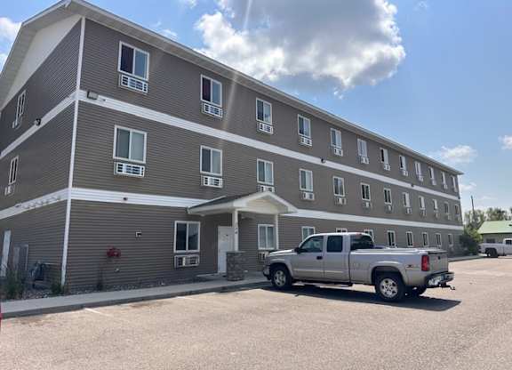 A silver truck is parked in front of a grey apartment building.