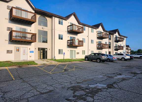 A parking lot in front of apartment buildings with cars parked.