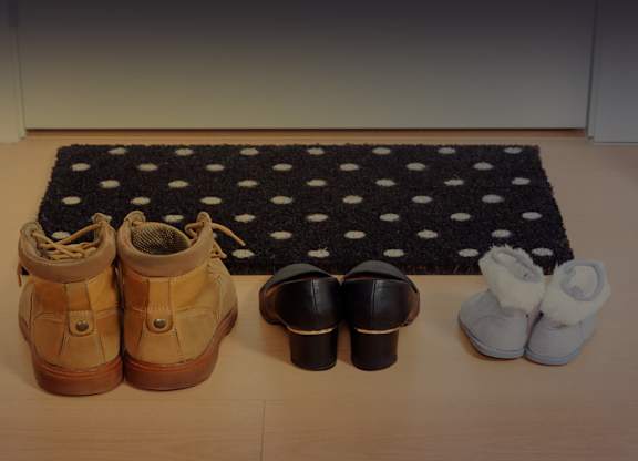 A pair of tan shoes, a pair of black shoes, and a pair of white shoes are arranged on a black and white polka dot rug.