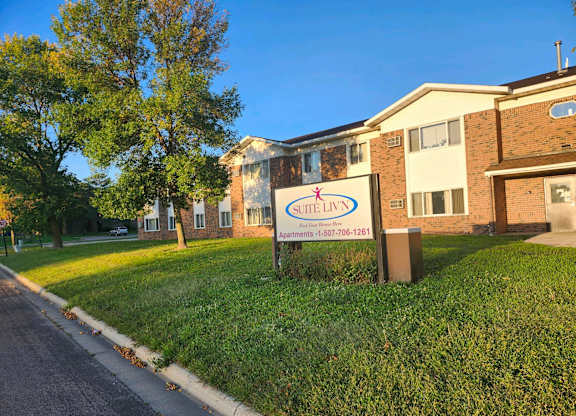 A sign for a place called "Sweet Liv'n" stands in front of a brick building.
