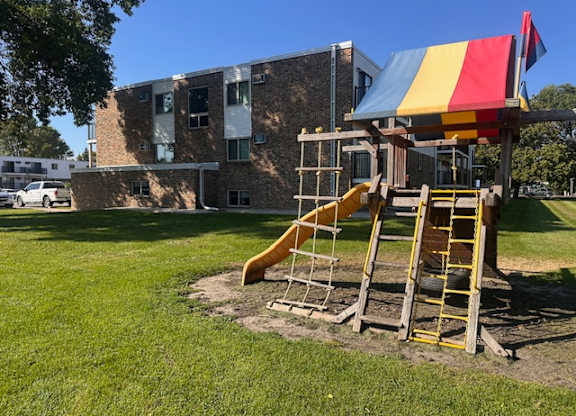 A playground with a yellow slide and a red, yellow and blue canopy.