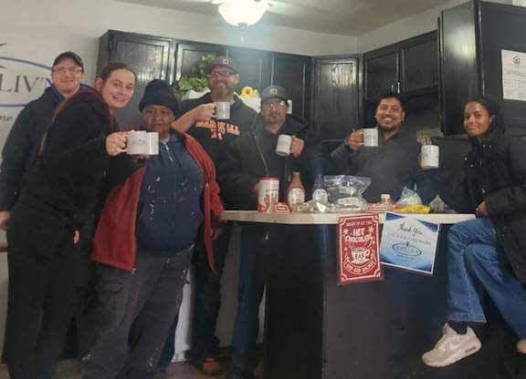 A group of people are gathered around a counter in a room with a sign that says "Suite Liv'n."