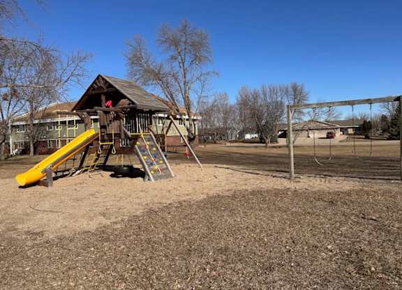 A playground with a yellow slide and a wooden structure.