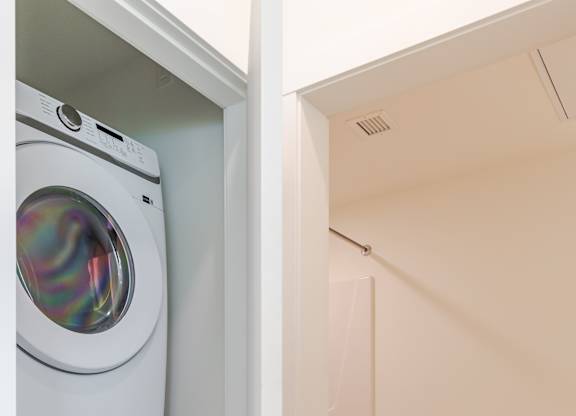 A white washing machine is in a small room with a toilet and a door.
