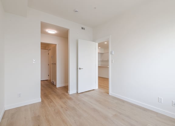 A room with white walls and wooden flooring with two doors.