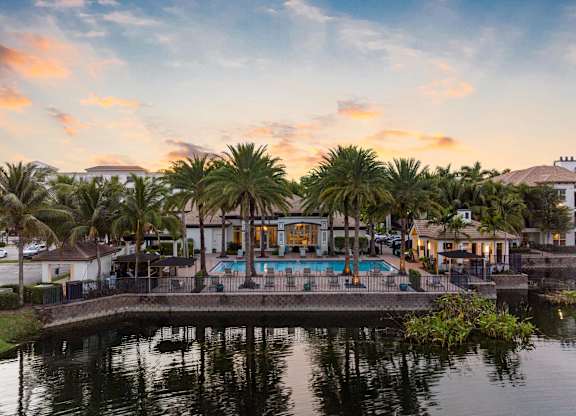 A beautiful view of a pool surrounded by palm trees at sunset.