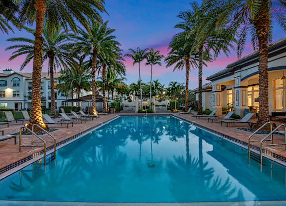 A swimming pool surrounded by palm trees and lounge chairs.