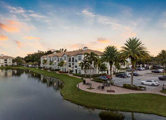 A serene lake surrounded by apartment buildings and palm trees under a clear sky.
