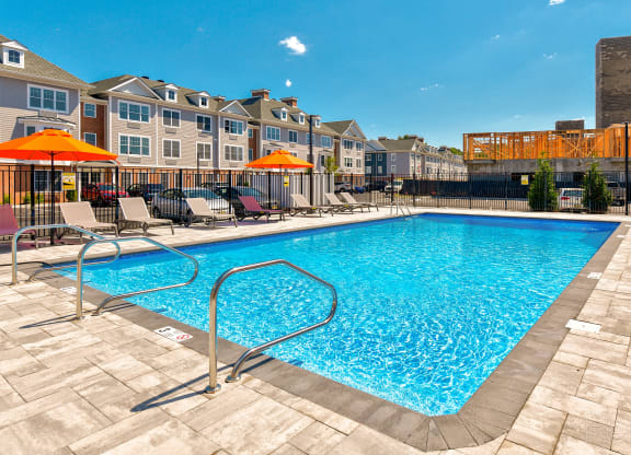 a swimming pool with chairs and umbrellas in front of apartment buildings at Solo at North Bergen, New Jersey