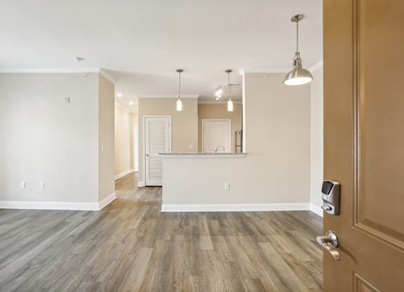 an empty living room with a kitchen in the background and a door open