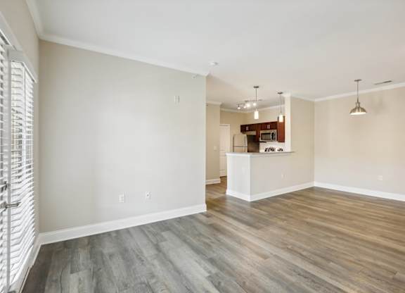 an empty living room with wood flooring and a kitchen