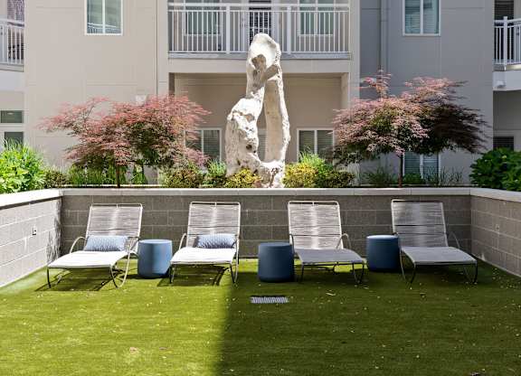 A sculpture of a person stands in a courtyard with chairs and plants.