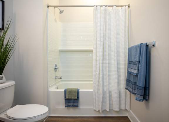 Modern bathroom at NOVI at Concord with bathtub and shower with white tile surround.