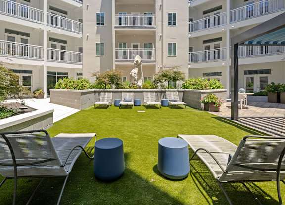 A small grassy area with two chairs and two trash cans in front of a building.