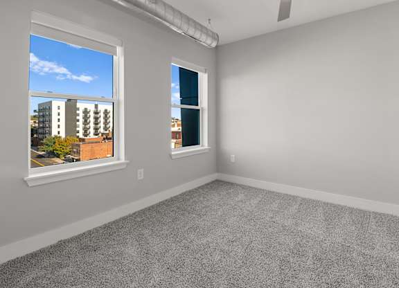 A room with a grey carpet and two windows.