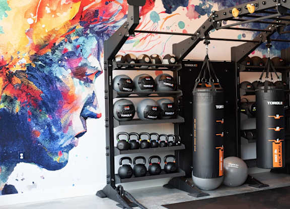 A gym with a punching bag, kettlebells, and a wall mural.
