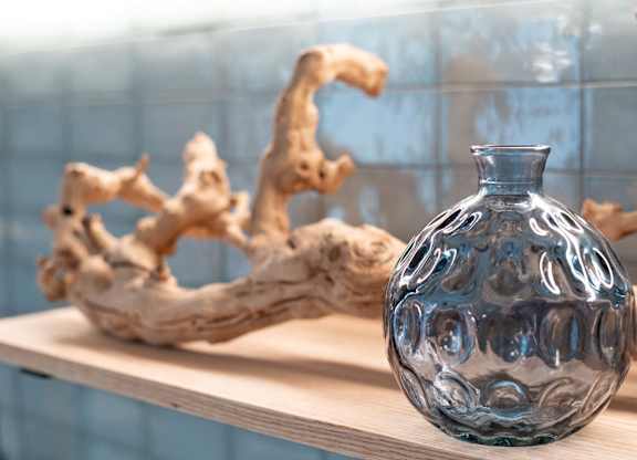 A blue glass vase sits on a shelf next to a piece of driftwood.