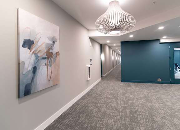 A hallway with a large painting on the wall and a carpeted floor.