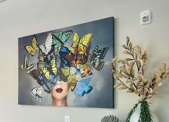 A painting of butterflies and flowers on a wall above a shelf with vases and plants.