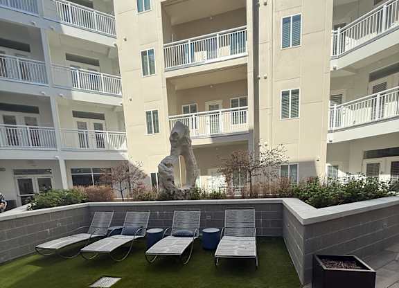 A sculpture sits in the middle of a grassy area in front of apartment buildings.