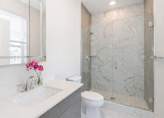 Modern apartment bathroom with glass shower and marble tile at The Rail North Bergen
