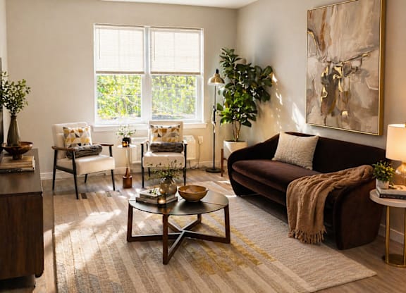 A living room at the Rail North Bergen with a brown couch, a coffee table, and a large painting on the wall.