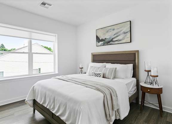 A bedroom with a large bed and a window overlooking a house at 10 N. Main Apartments, New Jersey