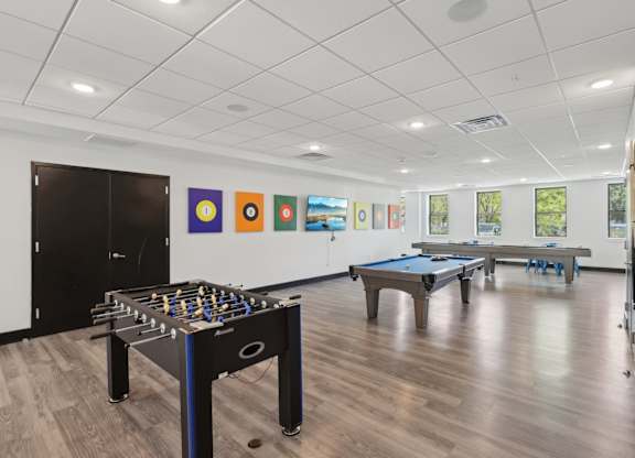 A foosball table is in the middle of a room with a pool table and pictures on the wall.