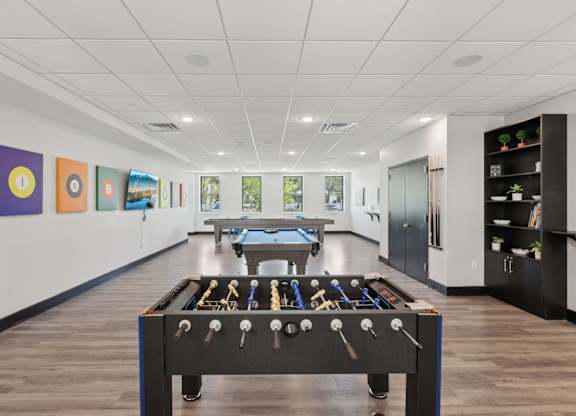 A foosball table is in the middle of a room with a pool table and pictures on the wall.