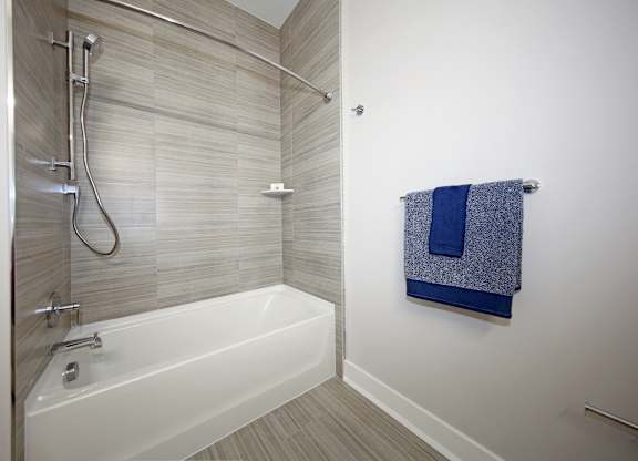 A white bathtub with a shower head and a towel hanging on the wall.
