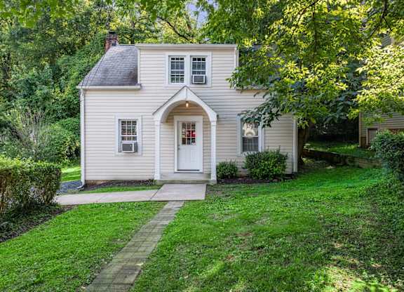 A small house with a white door and windows surrounded by greenery.
