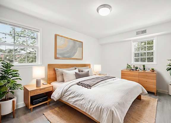 A bedroom with a bed, nightstand, and a plant.